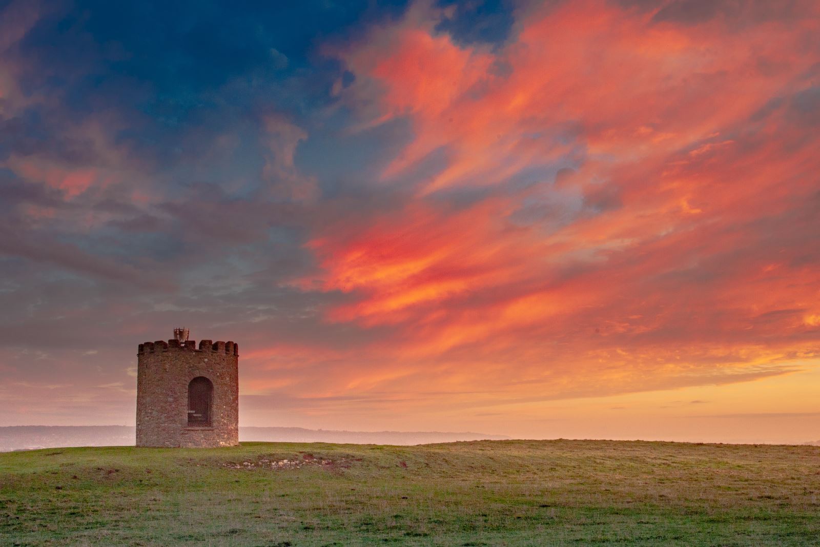 A stone beacon on a hill  under a blue, orange and red sky at sunrise